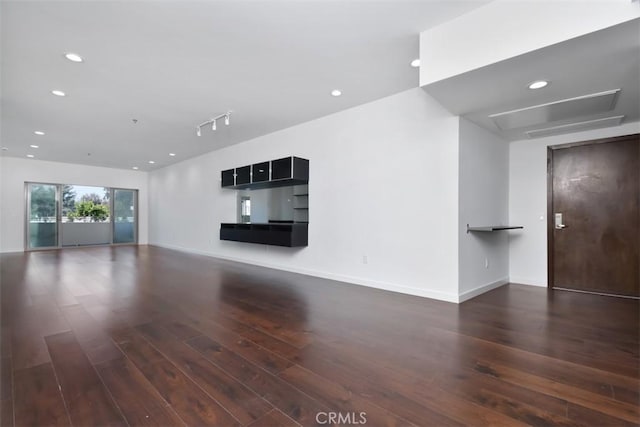 unfurnished living room featuring baseboards, attic access, recessed lighting, and wood finished floors