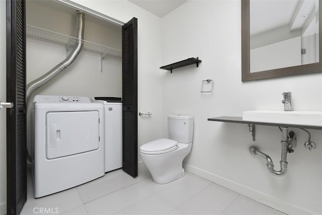bathroom with washer and dryer, toilet, a sink, tile patterned floors, and baseboards
