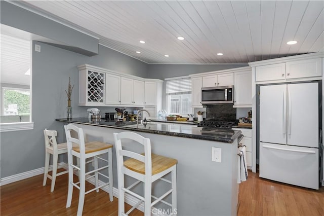 kitchen featuring freestanding refrigerator, white cabinets, light wood-type flooring, stainless steel microwave, and wooden ceiling