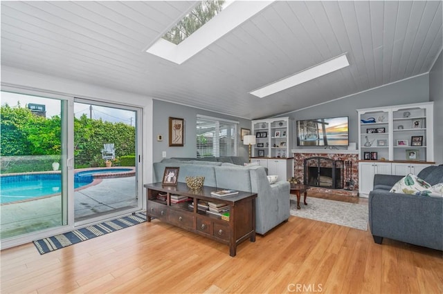 living room featuring lofted ceiling with skylight, a brick fireplace, and wood finished floors