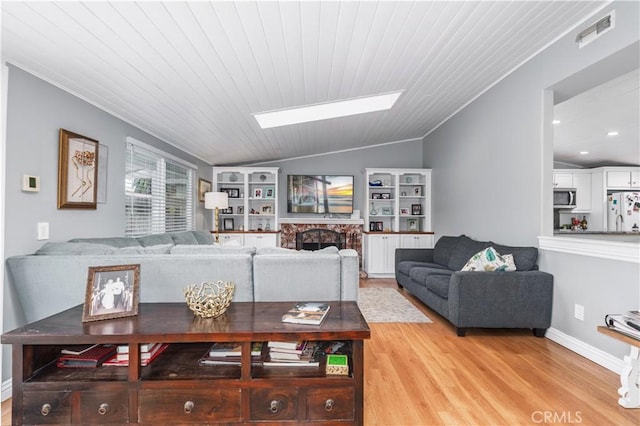 living area featuring baseboards, lofted ceiling with skylight, light wood-style flooring, and visible vents