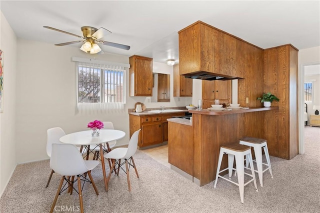 660 Stanley Ave, Long Beach, CA 90814 - kitchen featuring a peninsula, a kitchen bar, brown cabinetry, ceiling fan, and light colored carpet