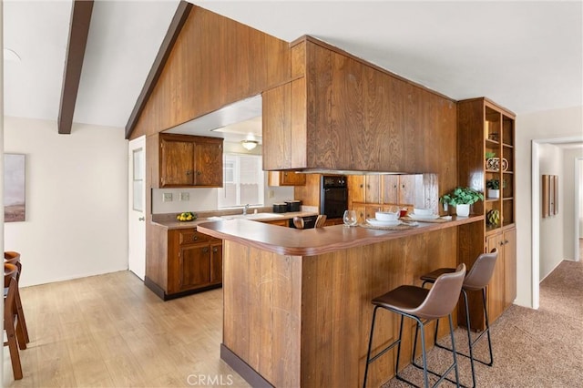 660 Stanley Ave, Long Beach, CA 90814 - kitchen featuring a peninsula, a breakfast bar area, a sink, black oven, and brown cabinetry