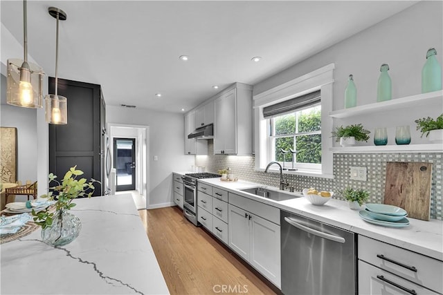 21820 Dumetz Rd, Woodland Hills, CA 91364 - kitchen featuring appliances with stainless steel finishes, under cabinet range hood, light stone counters, light wood finished floors, and backsplash