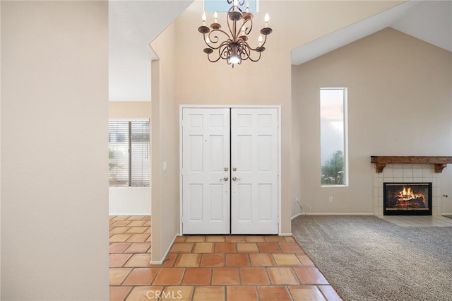 carpeted foyer with an inviting chandelier, a tiled fireplace, baseboards, and lofted ceiling