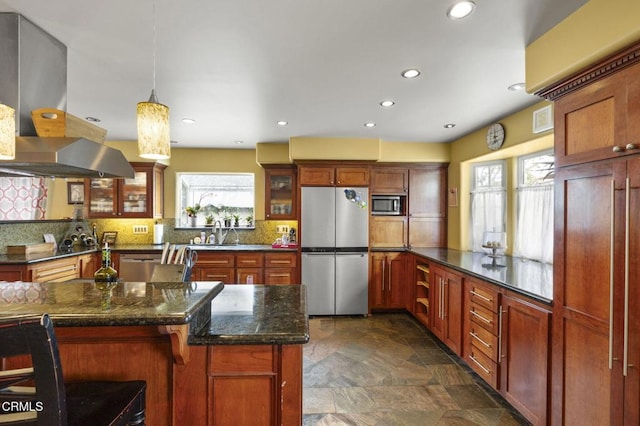 kitchen featuring island exhaust hood, stone finish floor, backsplash, glass insert cabinets, and appliances with stainless steel finishes