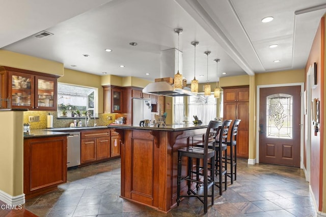 kitchen with a breakfast bar, dark countertops, island range hood, stone tile flooring, and fridge