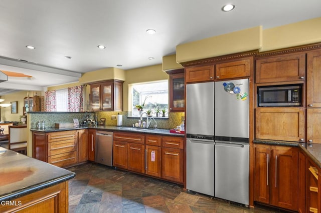 kitchen featuring stone finish floor, glass insert cabinets, a sink, decorative backsplash, and appliances with stainless steel finishes