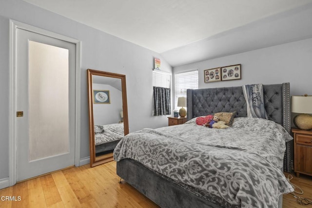 bedroom with light wood finished floors, lofted ceiling, and baseboards