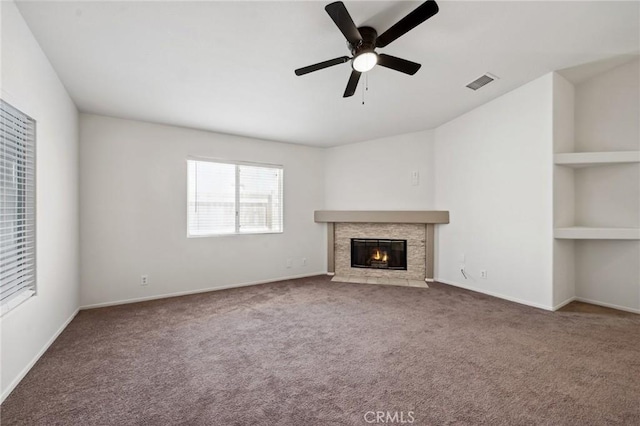 unfurnished living room featuring carpet flooring, visible vents, baseboards, ceiling fan, and a stone fireplace