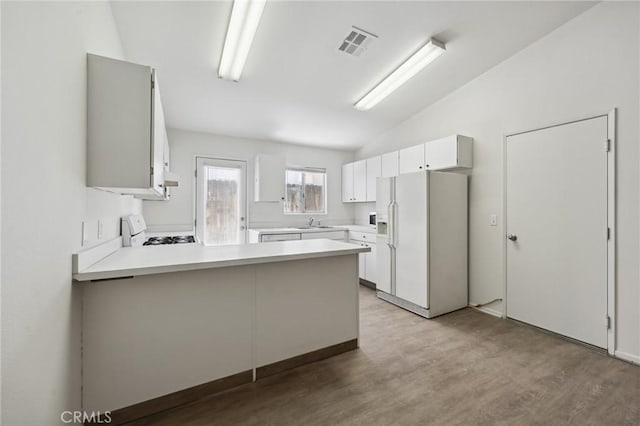 kitchen with white fridge with ice dispenser, lofted ceiling, gas range oven, visible vents, and a peninsula