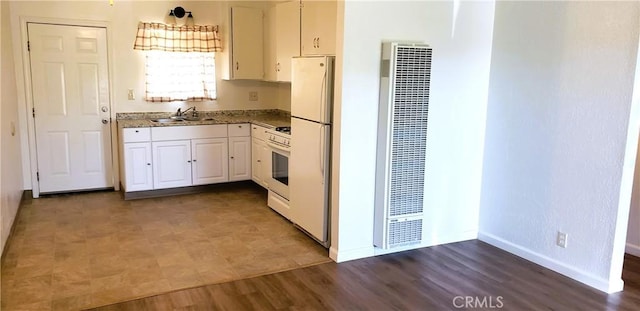 kitchen with wood finished floors, a heating unit, white cabinets, baseboards, and white appliances