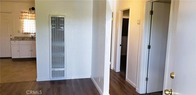 corridor featuring a heating unit, wood finished floors, baseboards, and a sink