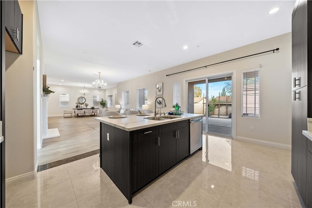 kitchen with dishwasher, dark cabinets, a sink, a chandelier, and an island with sink