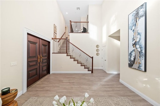 entrance foyer featuring light wood-type flooring, baseboards, a high ceiling, and stairs