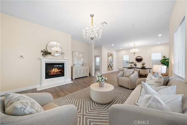 living room with wood finished floors, visible vents, an inviting chandelier, baseboards, and a glass covered fireplace