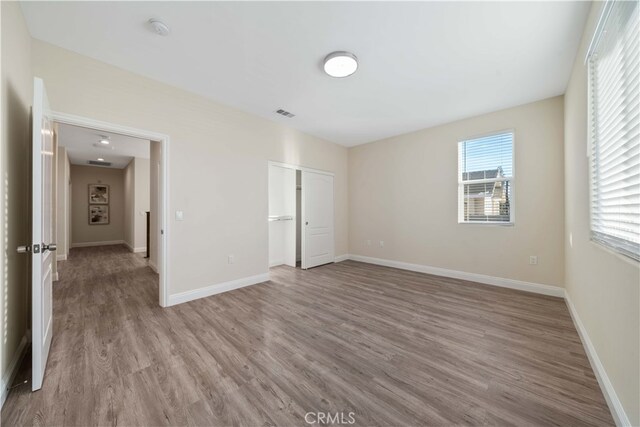 unfurnished bedroom with a closet, visible vents, wood finished floors, and baseboards