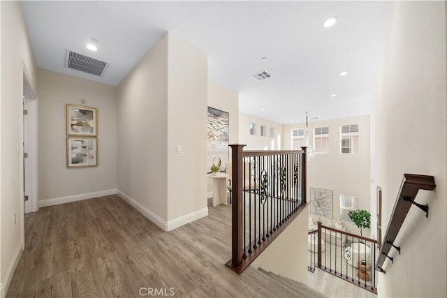 hall featuring baseboards, an upstairs landing, visible vents, and wood finished floors