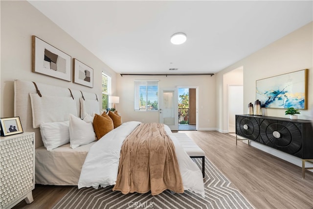 bedroom with baseboards, wood finished floors, access to exterior, and visible vents