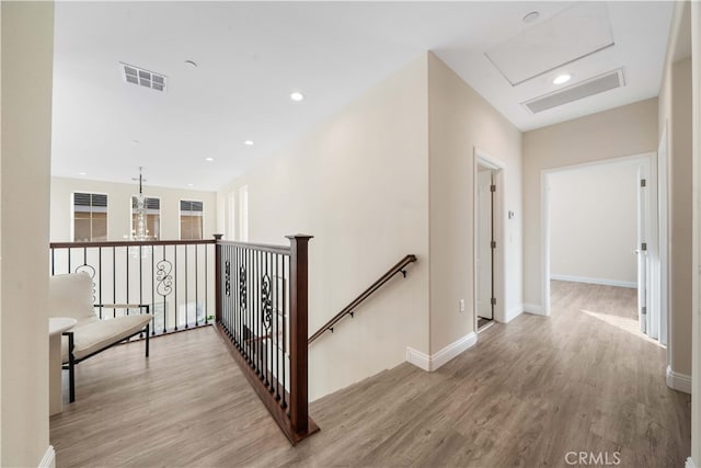 hallway with baseboards, an upstairs landing, visible vents, and wood finished floors