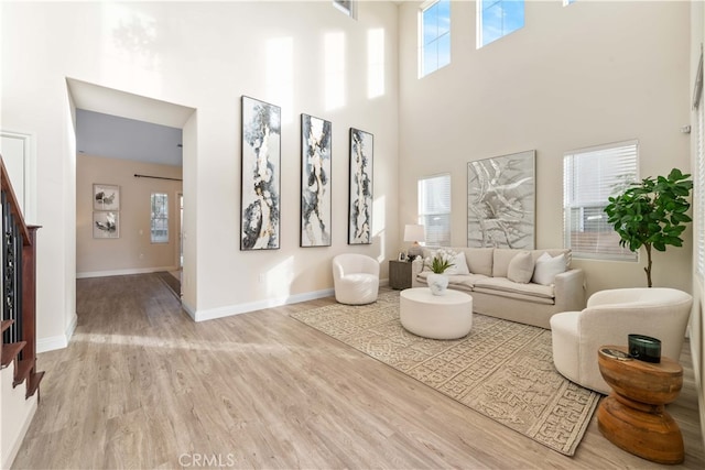 living room featuring a healthy amount of sunlight, wood finished floors, baseboards, and a high ceiling