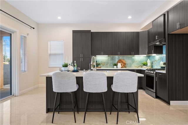 kitchen with a sink, tasteful backsplash, stainless steel gas stove, under cabinet range hood, and light countertops