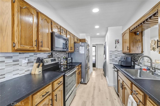 kitchen with a sink, brown cabinetry, tasteful backsplash, light wood finished floors, and appliances with stainless steel finishes