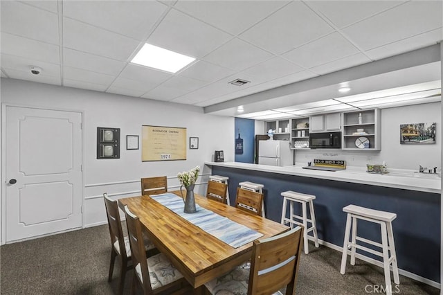 dining space with a paneled ceiling, dark carpet, and visible vents