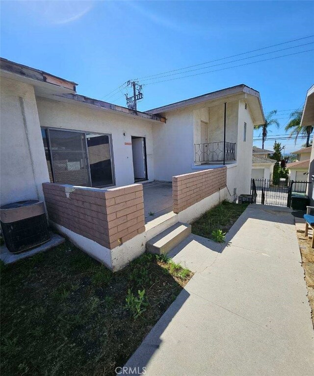 exterior space featuring a gate, fence, stucco siding, and central AC