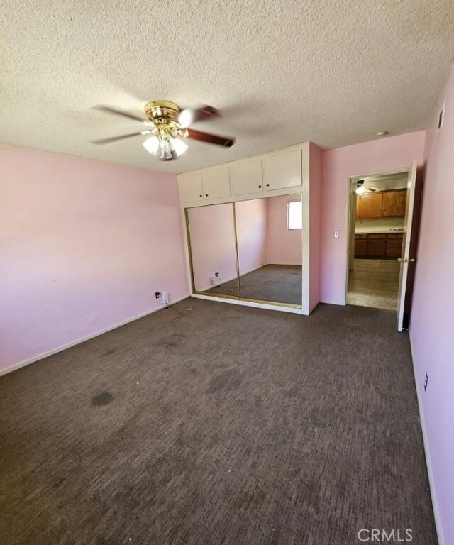 unfurnished bedroom featuring a textured ceiling, a closet, a ceiling fan, and dark carpet