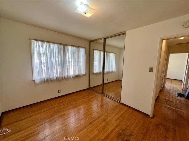 unfurnished bedroom with baseboards, a closet, visible vents, and wood finished floors