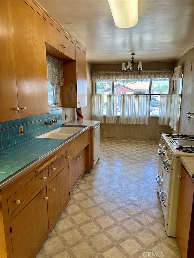 kitchen with a sink, white appliances, light floors, tile countertops, and an inviting chandelier