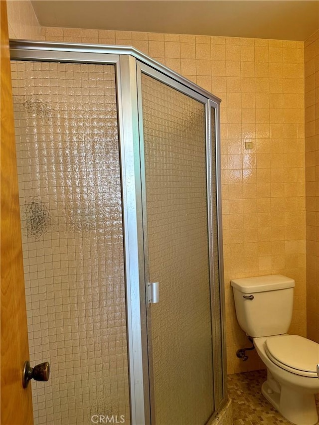bathroom with a stall shower, tile walls, toilet, and tile patterned floors