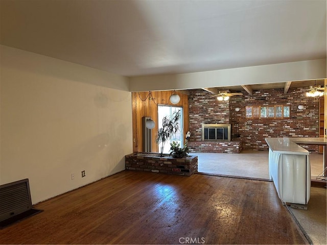 unfurnished living room featuring wood finished floors, a ceiling fan, a fireplace, brick wall, and visible vents