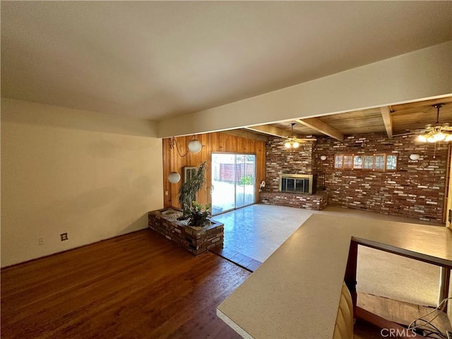 unfurnished living room featuring ceiling fan, a brick fireplace, beamed ceiling, and wood finished floors