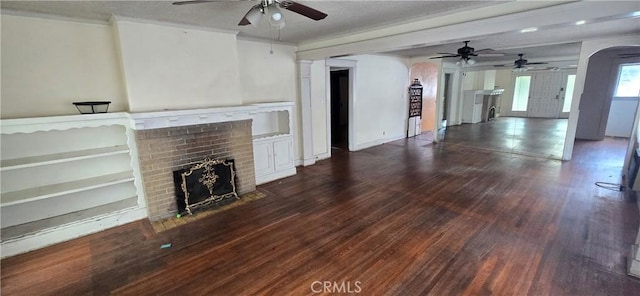 unfurnished living room featuring a brick fireplace, arched walkways, a ceiling fan, and wood finished floors