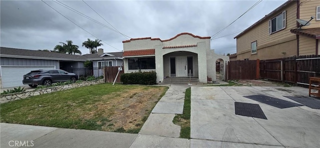 mediterranean / spanish house with a front lawn, stucco siding, and fence