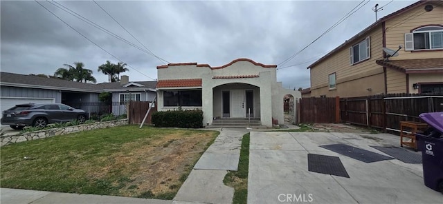 mediterranean / spanish-style home featuring stucco siding, fence, and a front lawn