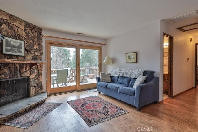 living room featuring hardwood / wood-style flooring, a stone fireplace, and visible vents