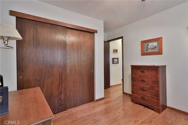 bedroom with light wood finished floors, a closet, and baseboards