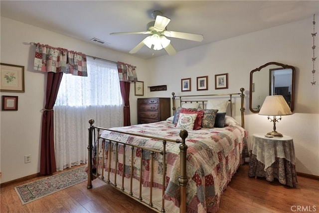 bedroom featuring a ceiling fan, visible vents, wood finished floors, and baseboards