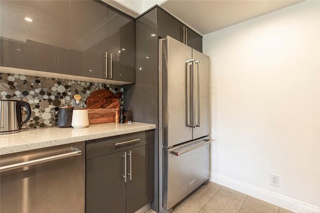 kitchen with light stone countertops, baseboards, light tile patterned floors, decorative backsplash, and appliances with stainless steel finishes