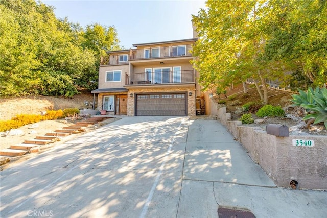 view of front of property featuring concrete driveway, stucco siding, an attached garage, and a balcony