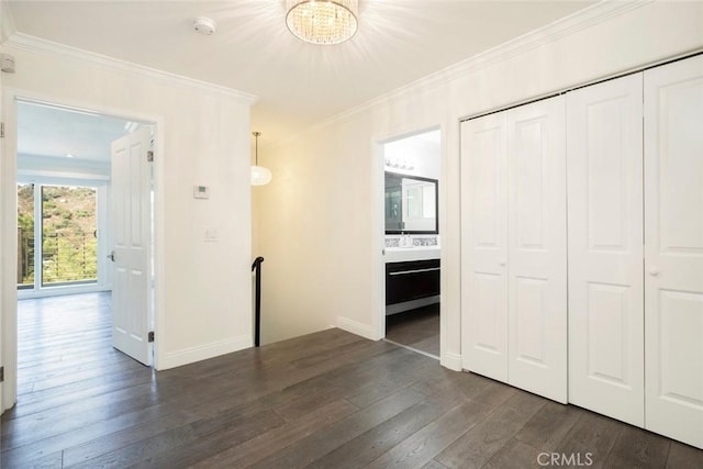 unfurnished bedroom with a closet, ornamental molding, dark wood-style flooring, an inviting chandelier, and baseboards