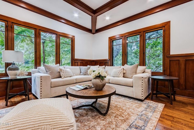 living area with wood finished floors, coffered ceiling, beam ceiling, a decorative wall, and wainscoting