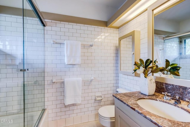 bathroom featuring a shower with shower door, vanity, tile walls, and toilet