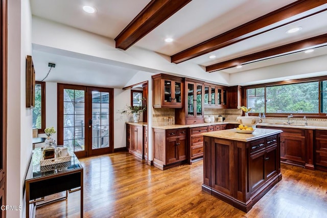 kitchen featuring french doors, glass insert cabinets, a sink, wood finished floors, and tasteful backsplash