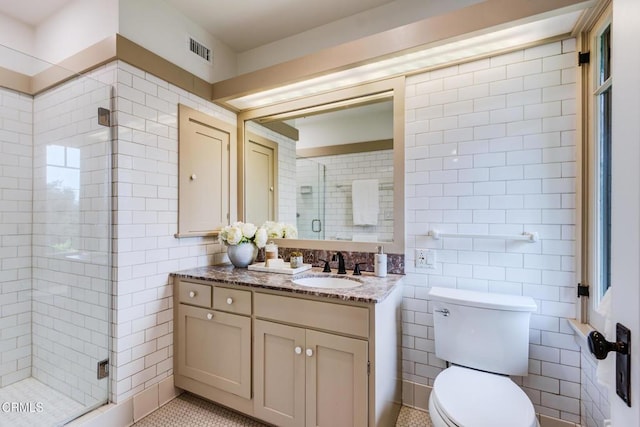 bathroom featuring a stall shower, tile walls, toilet, visible vents, and vanity