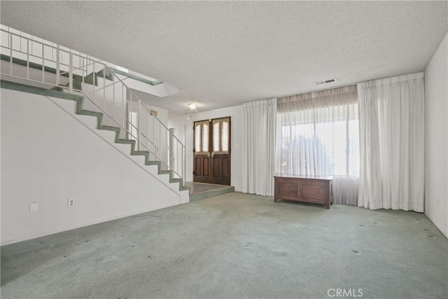 unfurnished living room with a textured ceiling, visible vents, stairway, and carpet floors