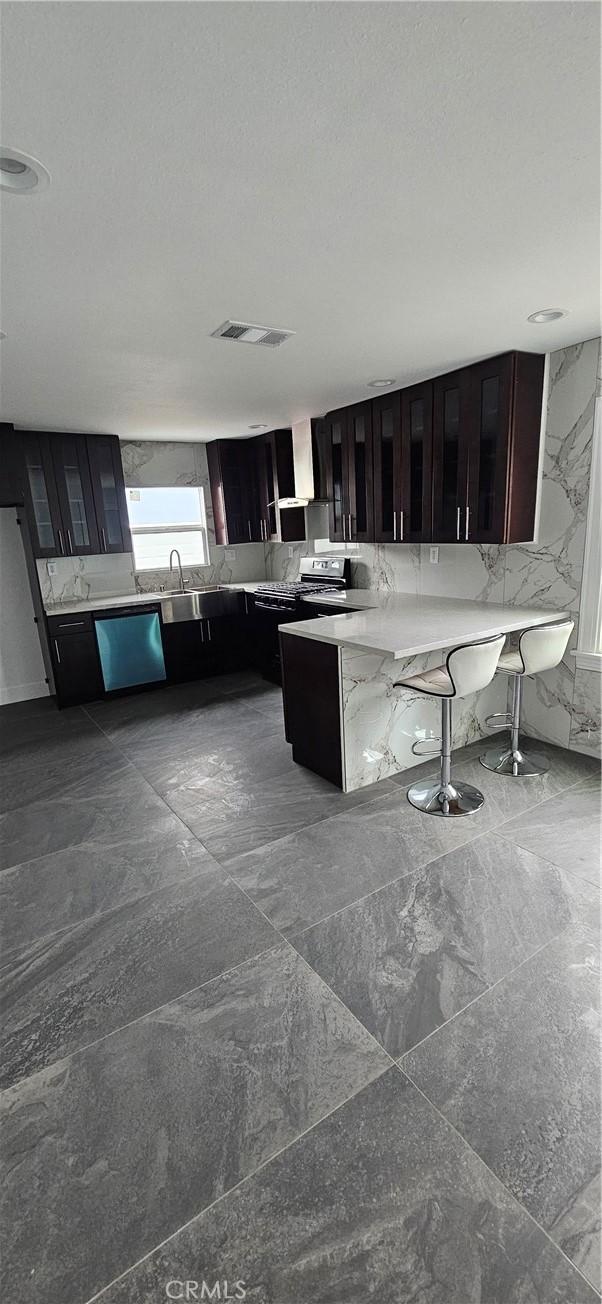 208 S Burris Ave, Compton, CA 90221 - kitchen featuring stainless steel dishwasher, a peninsula, light countertops, wall chimney exhaust hood, and a breakfast bar area